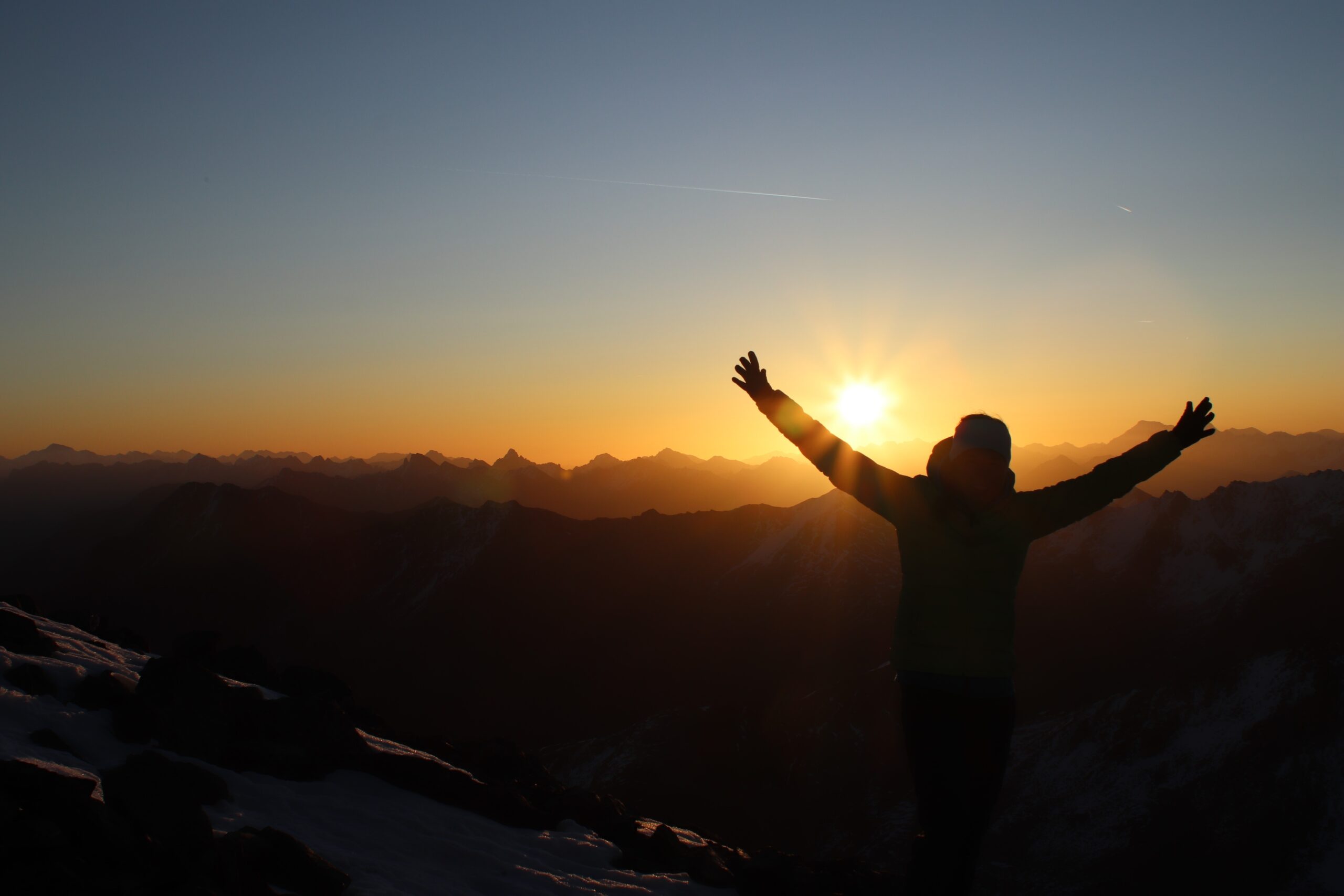 sabrina baetscher bei sonnenaufgang auf dem flüela schwarzhorn gipfel davos. die hände in die luft streckend und jubelnd